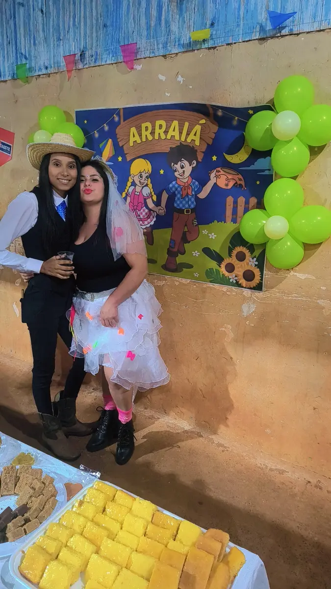 Organizadoras em frente ao painel do arraiá