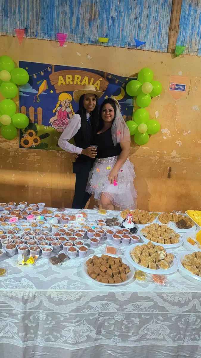 Mesa de alimentos e organizadoras da Festa Junina